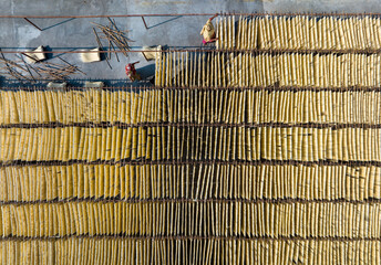 Bogura, Bangladesh - 22 April 2021: Aerial view of golden strips of food drying under the sun, laid out neatly in rows, contrasting with the dark figures tending to them.