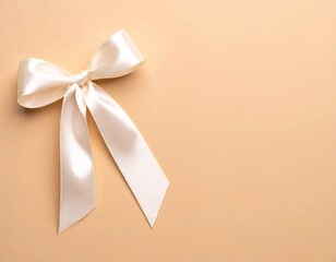 A close up of a satin ribbon bow in cream color against a peach colored plain background surface