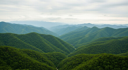 A panoramic view of rolling green mountains under a cloudy sky with a distant hazy mountain range