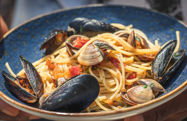 Spaghetti with clams and black mussels, fresh cherry tomatoes, parsley leaves and ground black pepper served in a blue ceramic plate