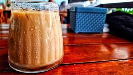 Milk Being Poured Into Iced Coffee on a wooden table. Fresh iced coffee with milk.  Cold coffee drink with ice cubes.