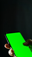 Close-up of right hand gripping smartphone with green screen, angled side view over dark...