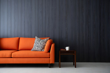 Orange sofa with patterned pillow and white mug on dark wood paneled wall couch living room