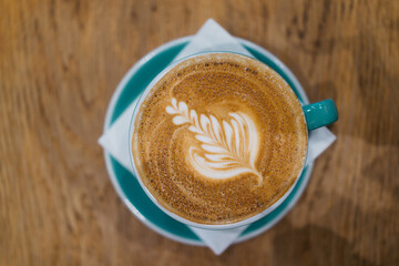 Artistic Coffee Latte with Intricate Leaf Foam Design in Turquoise Cup on Wooden Tabletop