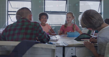 Collaborating elementary school students working around desk in classroom, with notebooks, pencils