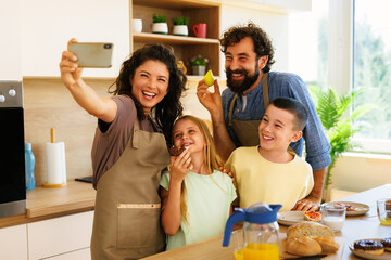 Cheerful family taking a selfie with smartphone while enjoying breakfast together in modern kitchen