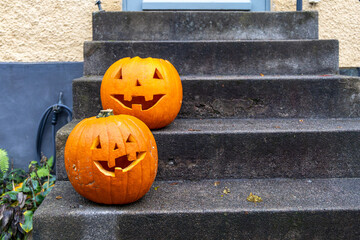 Two carved Halloween pumpkins with smiling faces sit on outdoor concrete steps. Both...