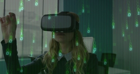 Woman wearing collared sweater using VR headset raising hand at office desk, with binary code
