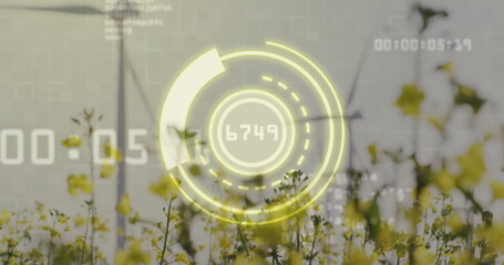 AR gauge displaying readout 6749 and timecode overlays over canola field with two wind turbines