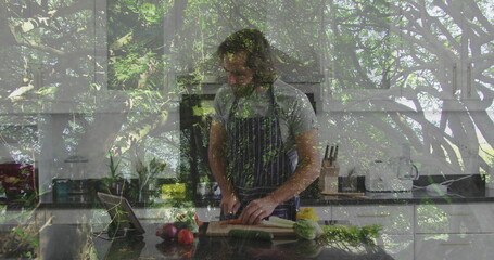 Adult man wearing striped apron slicing celery on kitchen island, with cutting board and tablet