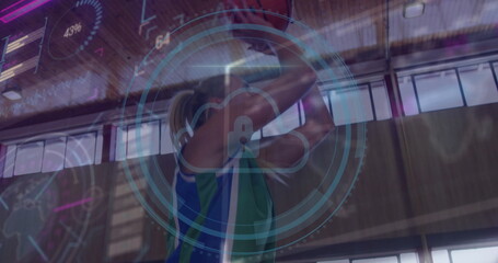 Female athlete holding basketball overhead in sports hall, with digital overlay and jersey