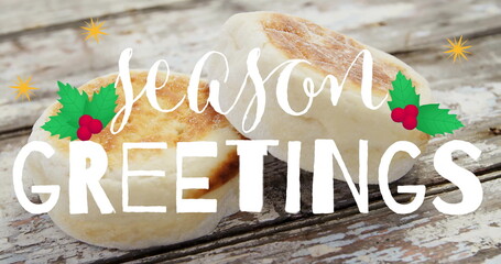Fototapeta premium Featuring two English muffins on rustic tabletop showing season GREETINGS text with holly and stars