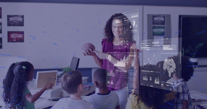 Holding brain model, teacher wearing magenta blouse pointing at holographic charts in classroom