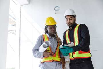 Construction engineers in safety helmets and reflective vests review building plans using tablet and blueprints, highlighting teamwork, planning and digital tools in construction management.