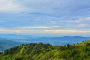 Obraz premium Vast mountain landscape under a partly cloudy sky, with a lush, green hillside in the foreground and a series of hazy, layered mountains receding into the distance. Related to mountain nature