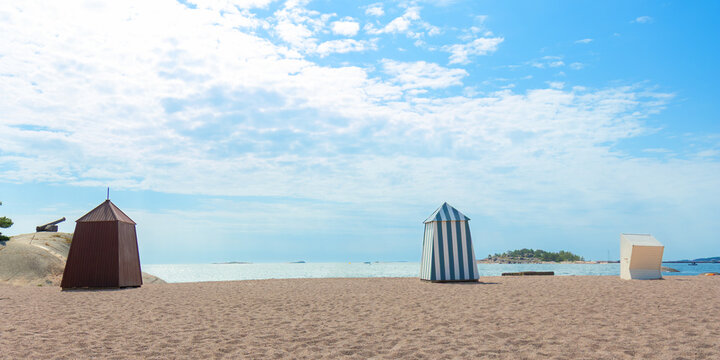 Sunny sandy beach in Hanko, Finland, with colorful iconic changing cabins, huts, booths, a cheerful Finnish Riviera vibe and relaxing seaside summer resort atmosphere with a sea view