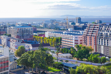 Panoramic cityscape of Cape Town, South Africa in a bright sunny day, showing modern apartment buildings, historic architecture, and lush greenery with the Atlantic Ocean in the background