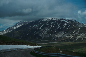 Dramatic Mountain Landscape with Winding Road, Snow-Capped Peaks, and Stormy Sky