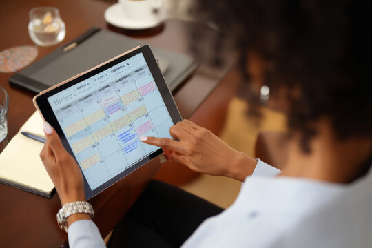 Mature Black woman scheduling international meetings, balancing time zones and appointments on a digital calendar