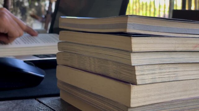 a person reading a book in front of a laptop with several stacks of books.