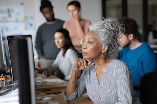 Middle-aged African-American woman reviewing tech support tickets with the IT team, discussing patterns in recent user issues