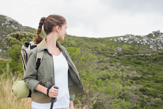 Fototapeta Backpack resting on grassy mountain slope with scattered rocks and low shrubs under cloudy sky