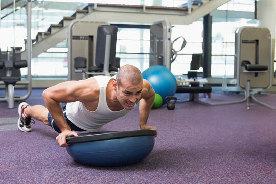 Man performing push-up on half-dome balance trainer at fitness center, engaging core muscles - Powered by Adobe