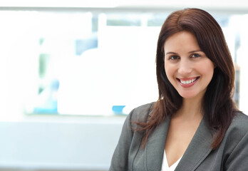 Obraz premium Female professional standing by office window wearing grey blazer and white blouse, copy space
