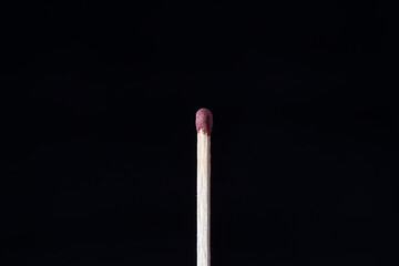 A single, unlit matchstick with a red head, centered vertically against a solid black
