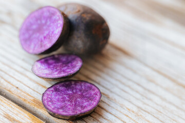 Bright cross-sections of purple potatoes displayed on rustic wooden boards, highlighting their deep color and natural marbling patterns.