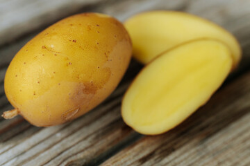 A whole yellow potato and two halves placed on a rustic wooden base, revealing a smooth, creamy interior and the natural texture of the skin.