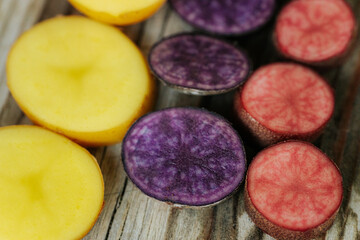 Cross-sections of yellow, purple and pink potatoes arranged on rustic wood, showcasing a variety of bright colors and smooth internal textures.