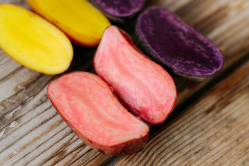 Six potato halves in bright yellow, pink and purple tones arranged on a wooden surface, showcasing their inner diversity. Space for text included.