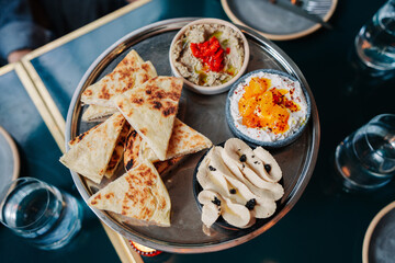 A platter of hummus, baba ghanoush, and pita bread with olives and hard-boiled eggs, served on a metallic tray.