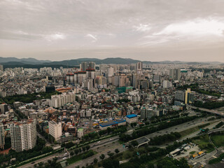 Obraz premium Aerial view of a sprawling cityscape with skyscrapers, highways, and mountains in the background under a cloudy sky.