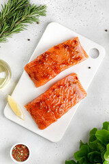 Marinated Salmon with sauce, red marinade, spicy. Fish steaks, slices. Raw uncooked salmon fillet fish with rosemary, lemon and pepper on white cutting board and grey background.