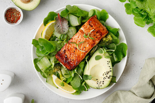 Baked roasted salmon steak with green healthy salad with avocado. Fresh diet dinner meal. Vitamin food concept on the plate and grey background.