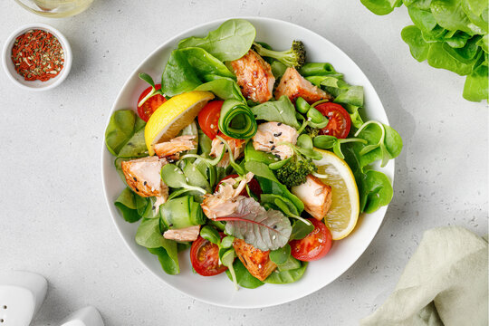 Healthy salad with pieces of baked salmon and green lettuce and tomatoes isolated on white background with clipping path. Fresh diet dinner meal. Fish summer salad. Vitamin food concept.