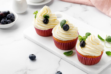 Cupcakes, muffins decorated with cream, berries and green mint leaves. Delicious homemade dessert. Pastry.