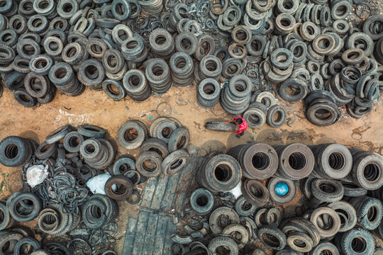 Bogura, Bangladesh - 12 April 2022: Aerial view of countless tires scattered across the ground, a stark landscape punctuated by the bright red of a lone figure amidst the rubbery chaos.