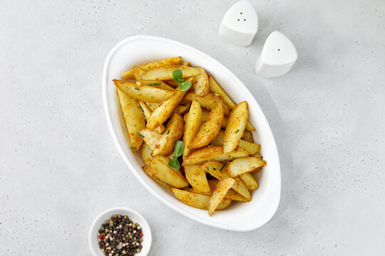 Baked potato wedges in white baking dish. Roasted potatoes with herbs and spices. Top view with copy space.