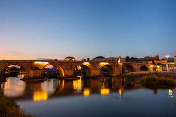 Old stone bridge over the Vardar River and Skopje city center at night, North Macedonia