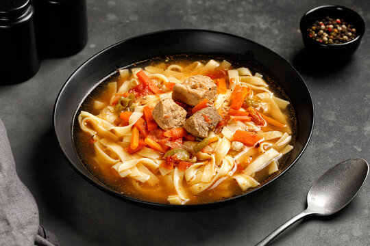 Lagman. The national Uzbek soup with noodles and pieces of meat, fried vegetables. Close up soup. Black plate and black background