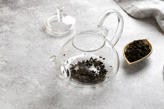 Teapot with green tea leaves on a gray background on a table with a napkin. Without water. Empty teapot