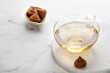 One glass cup or mug with green herbal tea  with sweets truffles on white marble background. Minimalism.