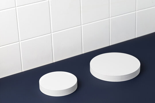 Podiums. White round podiums for presentation. Pedestals on blue background and tile wall. Two round podium