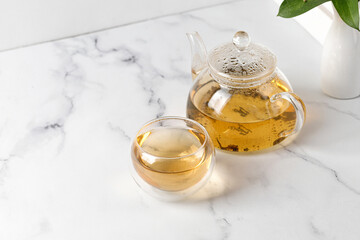 Double Wall Glass Cup with green tea and glass teapot on white marble background