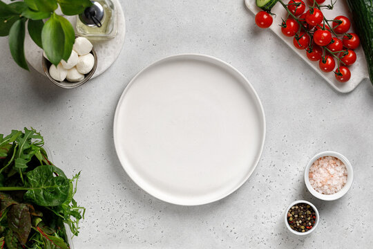 White empty plate for salad. Ingredients for salad cucumber slice, cherry tomatoes, mozzarella, mix salad. Top view.