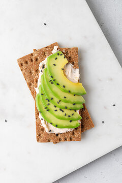 Green organic avocado slices on cream cheese on bread with black sesame seeds. Marble board