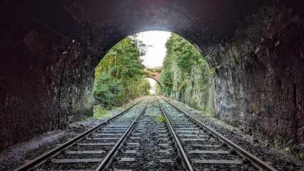 Naklejka premium Derelict deserted railway, light at the end of the tunnel. Crown Street arch entrance, Liverpool. Abandoned parallel straight train tracks inside dark bridge archway. Rail journey, horizon perspective